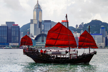 Traditional Chinese junk with red sails in Victoria Harbor, Hong Kong in China with panoramic city skyline views of Hongkong Central and Hong Kong skyscrapers and buildings