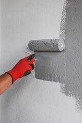 The painter paints the outer wall of the building with a gray paint roller - facade work - painting...