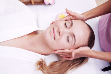 Obraz na płótnie Canvas Asian Massage therapist woman is making traditional head and facial treatment massage to Caucasian female is laying on bed at alternative medicine healing spa Center in Thailand.