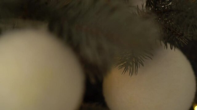 Closeup view video of green branches of Christmas tree decorated with white and golden decorative balls.