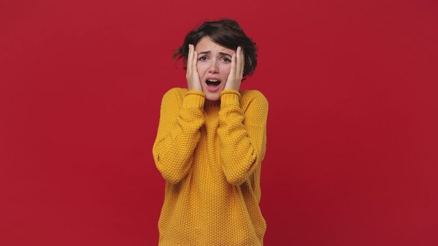 Sad Shocked Tired Young Woman 20s Years Old In Yellow Sweater Look Camera Put Hands On Head Say Ask What Expressive Gesticulating Isolated On Red Background Studio. People Emotions Lifestyle Concept