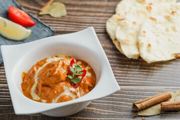 Butter chicken bowl and naan bread on wooden table. Curry - Meal, Indian food.