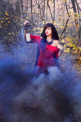 Fototapeta na wymiar A beautiful dark-haired woman in a red dress stands in gray smoke with a lantern in her hands.