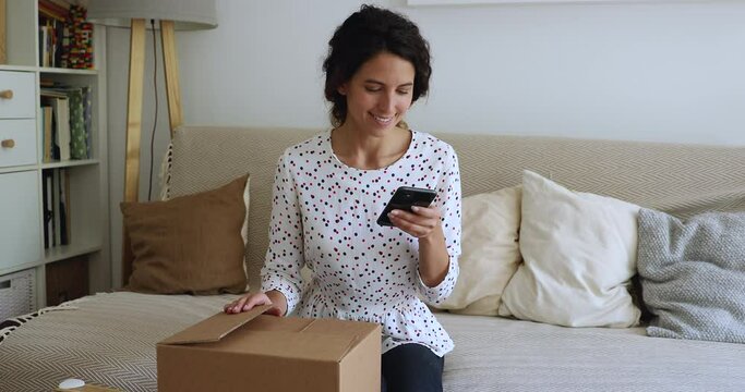 Woman sit on couch holds cellphone prepare package box to relatives, order courier to home through modern comfort on-line application. Easy goods return, using quick services of parcel sending concept