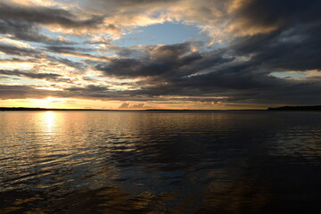 Sunset sun in the cloudy sky an over the calm surface of the lake water