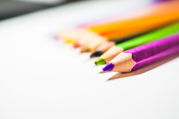 Colored pencils for drawing, well sharpened, lie in a row on a white background.