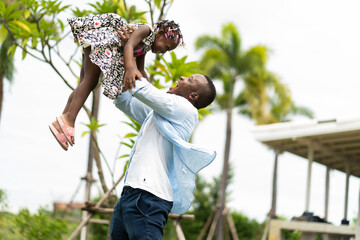 happy african american father playing with little daughter in green park.