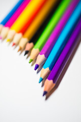 Colored pencils for drawing, well sharpened, lie in a row on a white background.