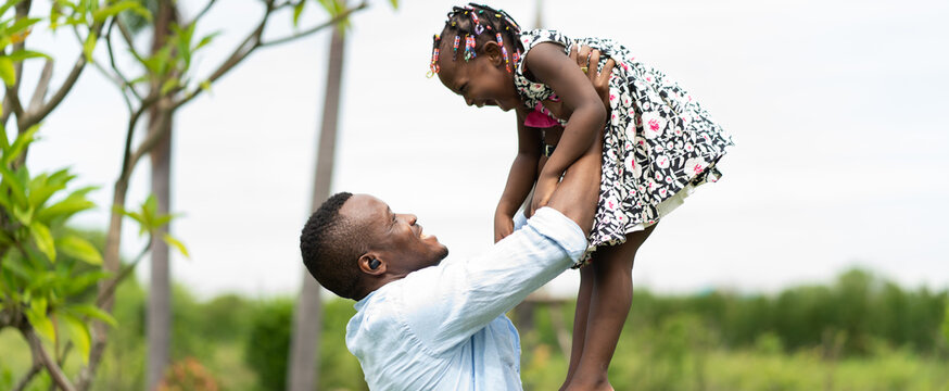happy african american father playing with little daughter in green park.