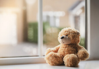 High key light sad teddy bear sitting near windowing sunny day, Lonely brown bear sitting alone at home, Concept to social distancing , stay at home and prevent spread of virus and disease in Children