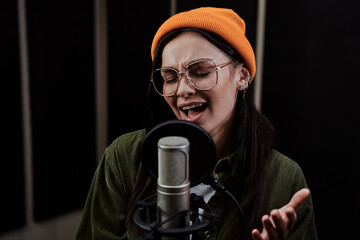 Portrait of young woman, hip hop artist enjoying the process of singing into a condenser microphone...