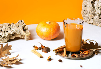 A pumpkin smoothie on an orange background stands on a metal plate, next to it lies a pumpkin,...