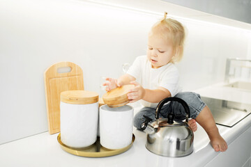 little girl kids European appearance child playing with toys dishes in the kitchen. happy mood, cozy apartment, daylight, stylish white kitchen