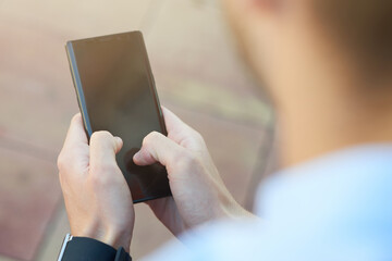 Rear view of a man using smartphone while spending time outdoors, focus on mobile phone