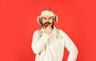 Caring fur garments. Winter fashion concept. Warm hat for cold weather. Sheep fur. Bearded funny hipster. Perfect accessory. Bearded man wear hat with ear flaps red background. Soft furry accessory