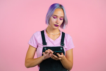 Hipster woman sms texting, using app on smartphone. Pretty girl with colorful hair surfing internet with mobile phone. Pink studio portrait.