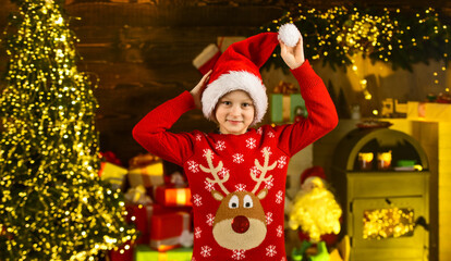 December tradition. Favorite day of year. Child happy excited near christmas tree. Merry christmas. Happy childhood concept. Kid wear santa hat and christmas sweater. Santa brought me gifts