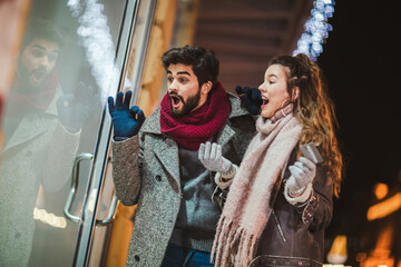 Couple with gift bag on Christmas lights background during walking in the city at evening. Window...