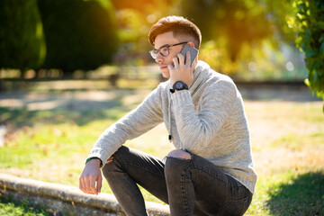 Young man in gray sweater in the park about talking on the phone and drinking coffee. Copyspace