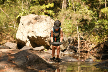 Young boy using pan to search for gold in creek, rural Australia