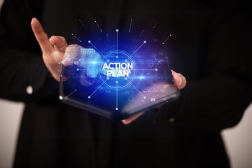 Businessman holding a foldable smartphone with ACTION PLAN inscription, new business concept