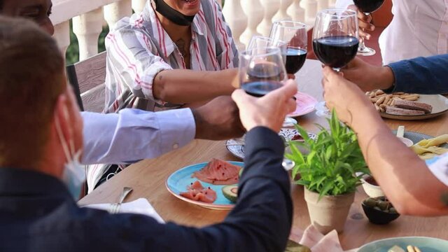 Young multiracial people cheering with wine while wearing protective masks - Dinner beetwen friends and lifestyle concept during coronavirus outbreak - Slow Motion
