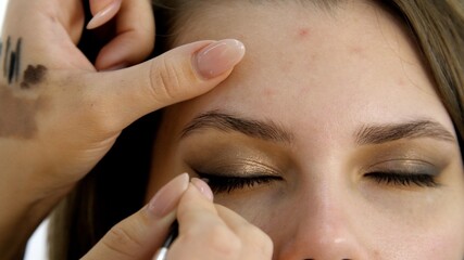 Makeup artist applying professional make-up to the eyes and eyelashes of the young woman....