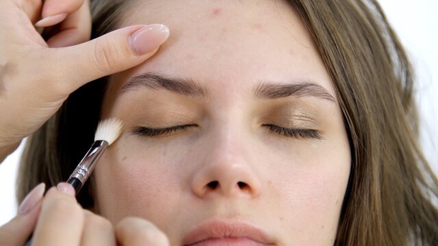 Attractive Female Face Of A Brunette Well-groomed Woman. Master Applies Makeup With A Special Brush In A Beauty Salon. Beauty Industry Of Cosmetics Backstage Of Professional Makeup. Female Eyes 