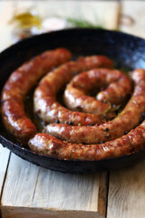 Selective focus. Fried homemade sausages in a frying pan on a wooden surface. Delicious Bavarian sausages.