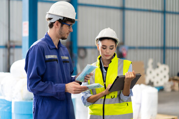 Female Inventory Manager checking stock on Digital Tablet. Man warehouse worker with hard hat safety helmet at storage buildings