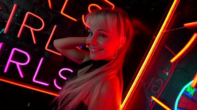 joyful go-go dancer woman is flirting with camera, portrait against signboard of nightclub with neon lights
