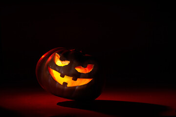 illuminated halloween pumpkin with leaning evil face on a dark background in red tones