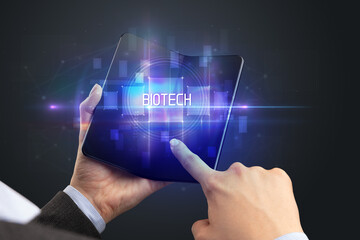 Businessman holding a foldable smartphone with BIOTECH inscription, new technology concept