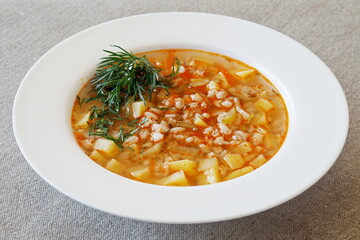 Soup with pickles, barley and vegetables on a linen tablecloth.