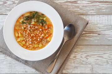 Soup with pickles, barley and vegetables on a wooden table.