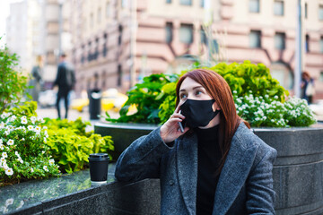 Fototapeta premium Redhead woman in protective mask talking on a smartphone in downtown. Business during coronavirus concept.