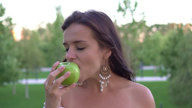 Attractive young woman eating a green apple outdoors