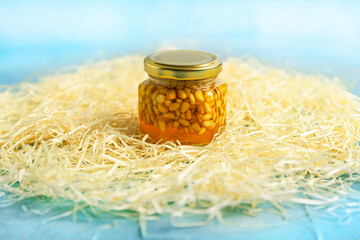 Jar of honey with nuts and honey spoon in a wooden box with sawdust, top view