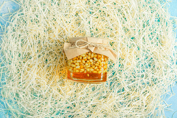 Jar of honey with nuts and honey spoon in a wooden box with sawdust, top view