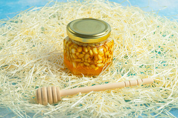 Jar of honey with nuts and honey spoon in a wooden box with sawdust, top view