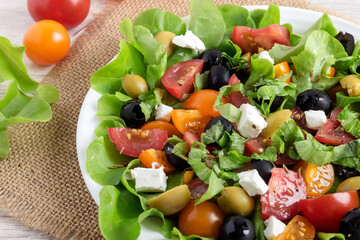 Appetizing fresh vegetable salad with tomatoes, olives, feta and green lettuce on a white plate.