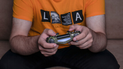 Fototapeta premium Male hands with game joystick, gamepad. The young guy is playing the console. Close up of man hands playing the video game at home. 