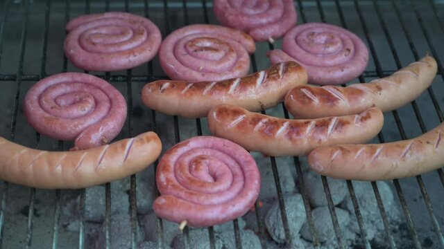 Sausages are twisted with tongs on a grill