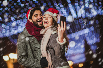 Fototapeta premium Young beautiful couple with Santa hats make selfie photo outdoor.