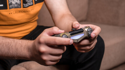 Fototapeta premium Male hands with game joystick, gamepad. The young guy is playing the console. Close up of man hands playing the video game at home. 