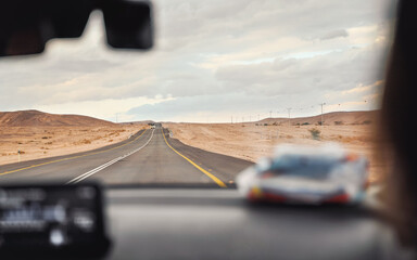 Car driving through desert landscape on overcast day, view from passenger seat, blurred dashboard foreground, roadtrip concept