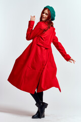emotional woman in a red coat and with a hat in full growth on a light background black boots pose...