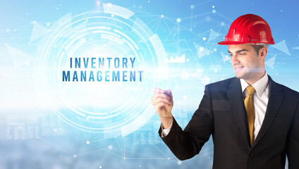 Handsome businessman with helmet drawing INVENTORY MANAGEMENT inscription, contruction business concept