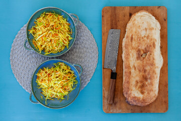 Ready stir-fry salad dish made in wok in two bowls. Board with white puri bread and modern Damascus...
