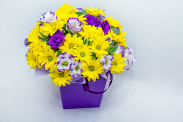 Beautiful bright colorful bouquet with yellow chrysanthemum and purple eustoma flowers in a box on white background